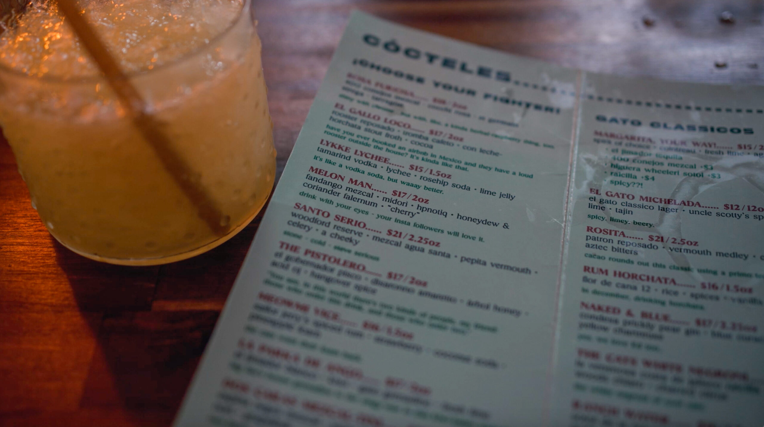 Cocktail glass and menu on a wooden table at El Gato Gab Gab in Vancouver.