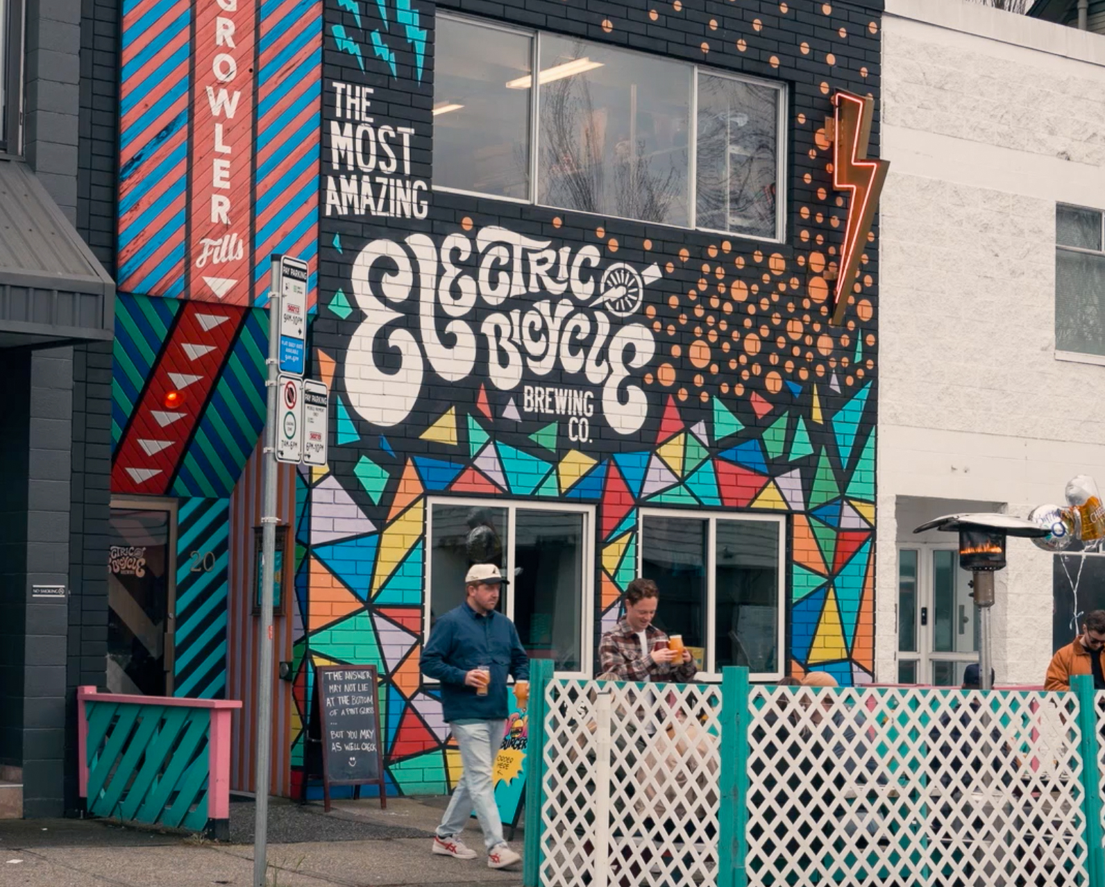 Bright, geometric mural outside Electric Bicycle Brewing Co. with a pedestrian walking by.