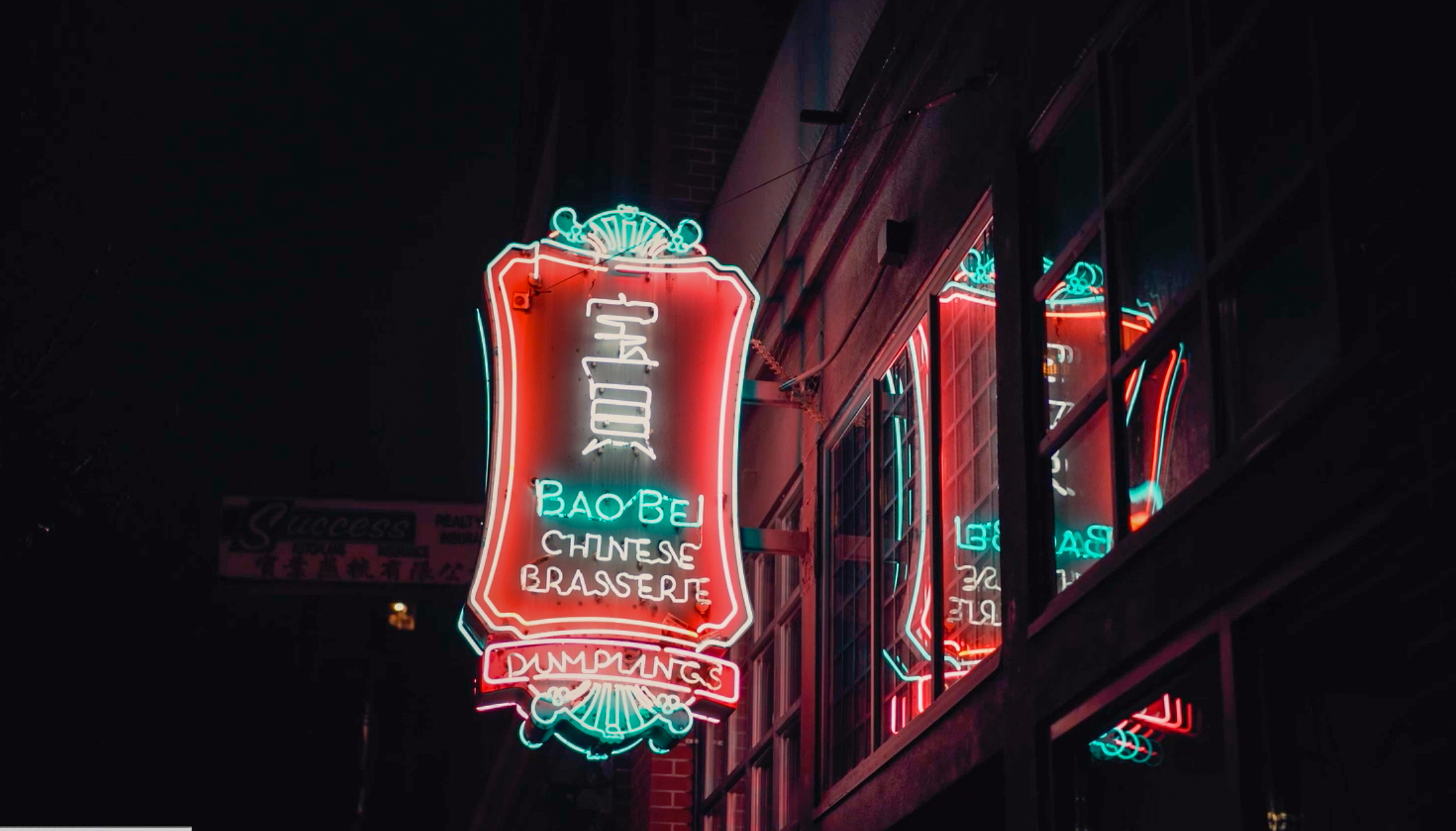 Neon sign for Bao Bei Chinese Brasserie glowing over a dimly lit Vancouver street at night.