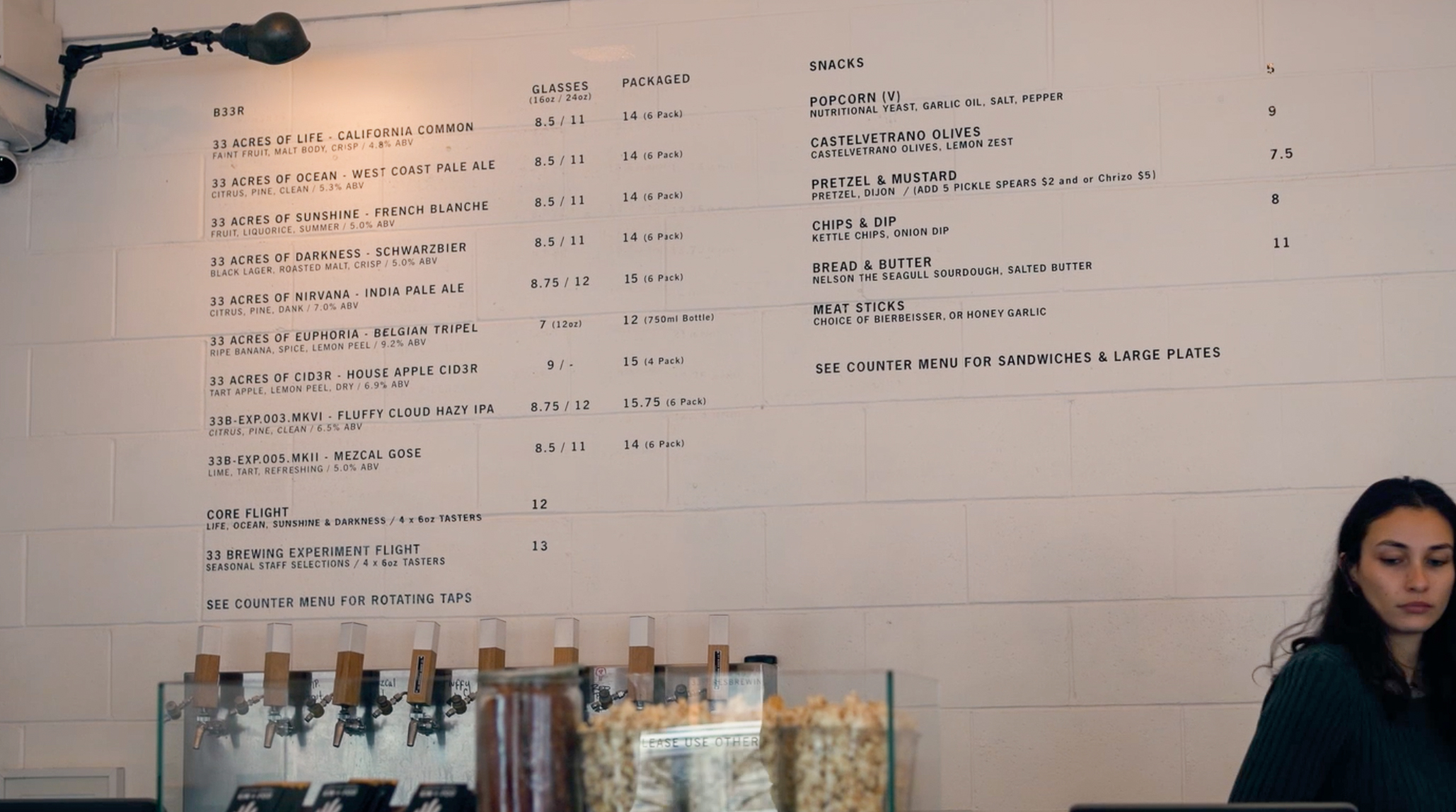 Minimalist taproom counter at 33 Acres Brewing in Vancouver, with a clean menu wall and bartender at the register.