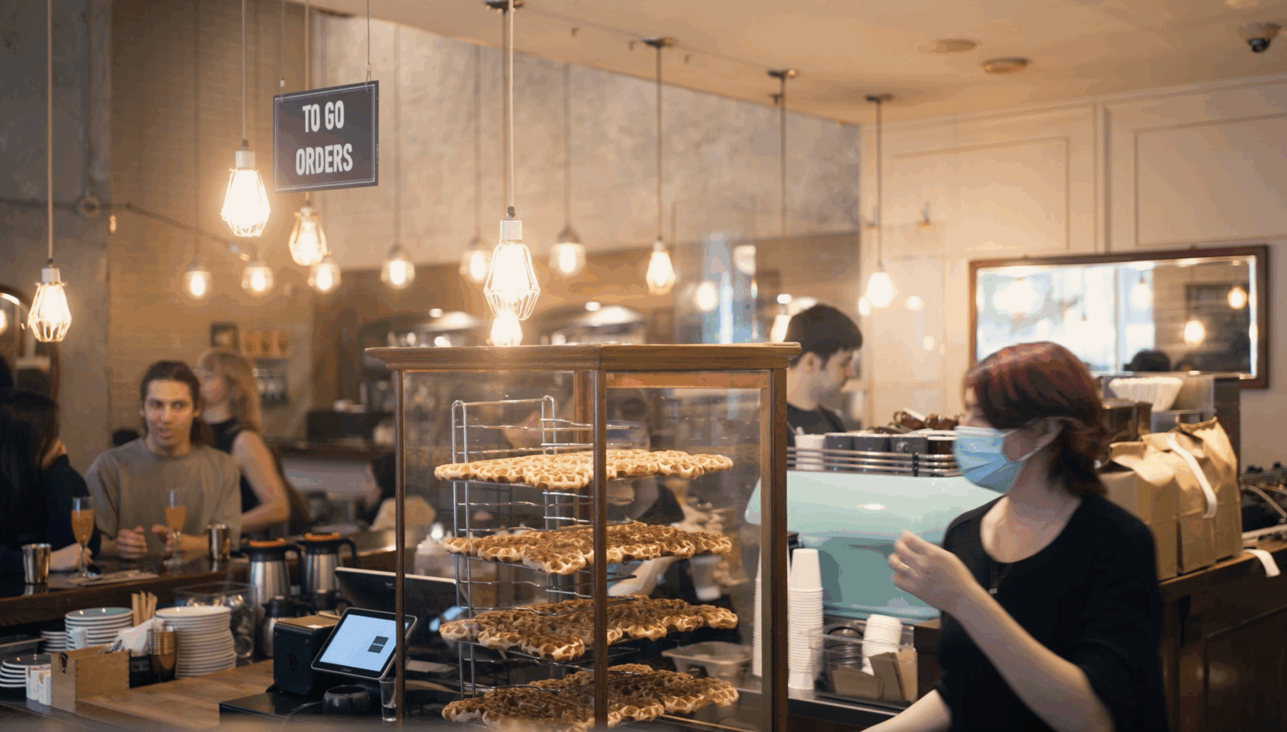 Staff behind the pastry counter at Cafe Medina in Vancouver, with warm lighting and a bustling brunch crowd.