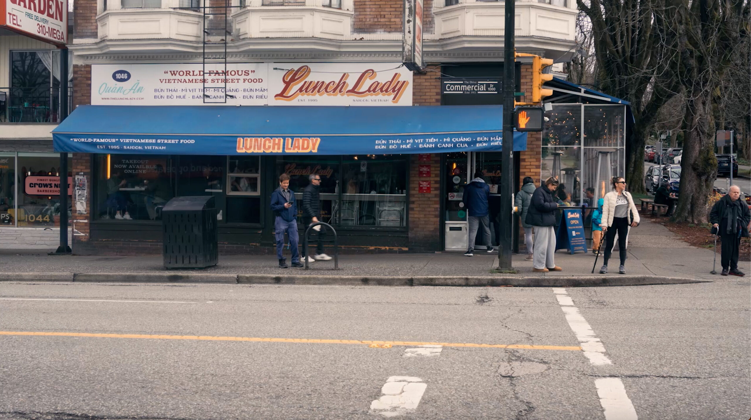 Street view of The Lunch Lady restaurant in Vancouver, featuring its blue awning and corner location with pedestrians walking by.