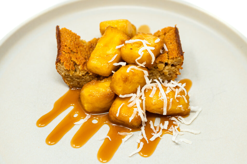 A golden pineapple almond loaf cake topped with caramelized pineapple and crumb topping, sliced and served on a white plate.