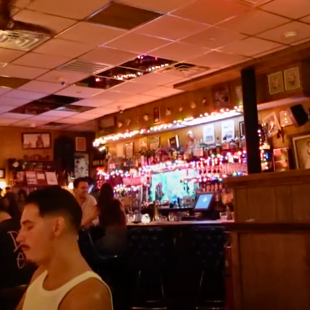 People sitting at the bar inside The Flower Shop, with colorful lights and framed photos covering the walls.