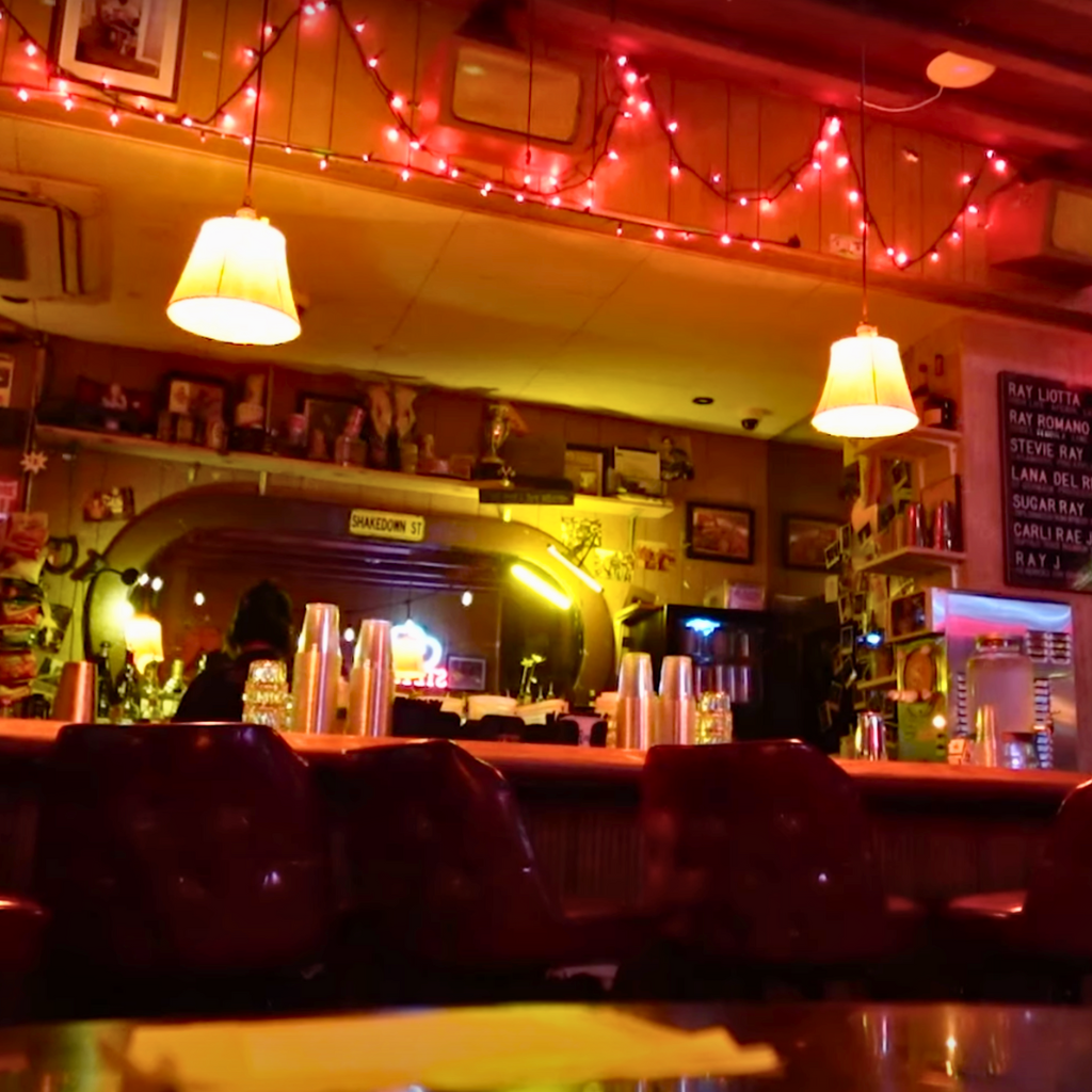 Interior of Ray’s bar glowing with red and yellow neon, vintage decor, and cozy booth seating.
