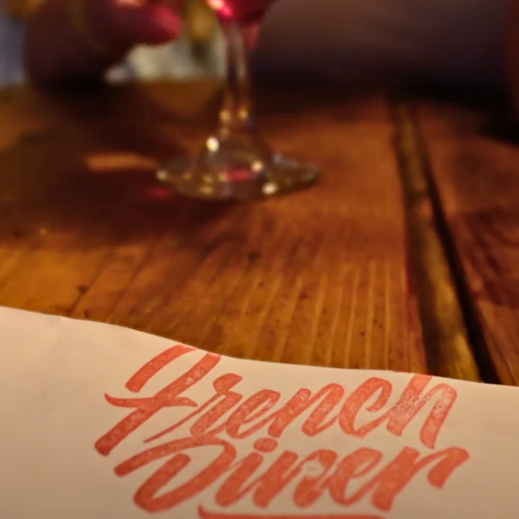 Close-up of a table setting at Le French Diner, showing the logo on a white menu and a blurred wine glass.