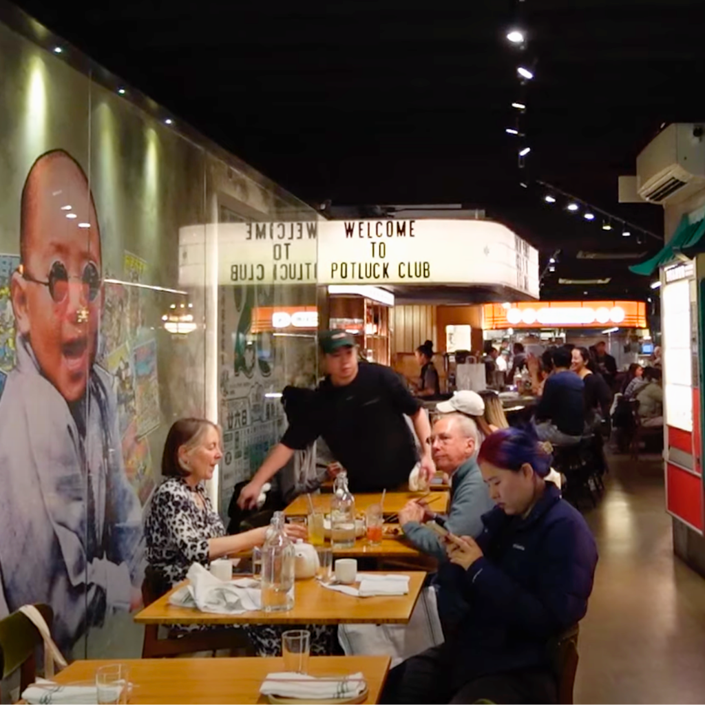 Interior of Potluck Club showing diners, neon signage, and a retro movie poster wall in Chinatown NYC.