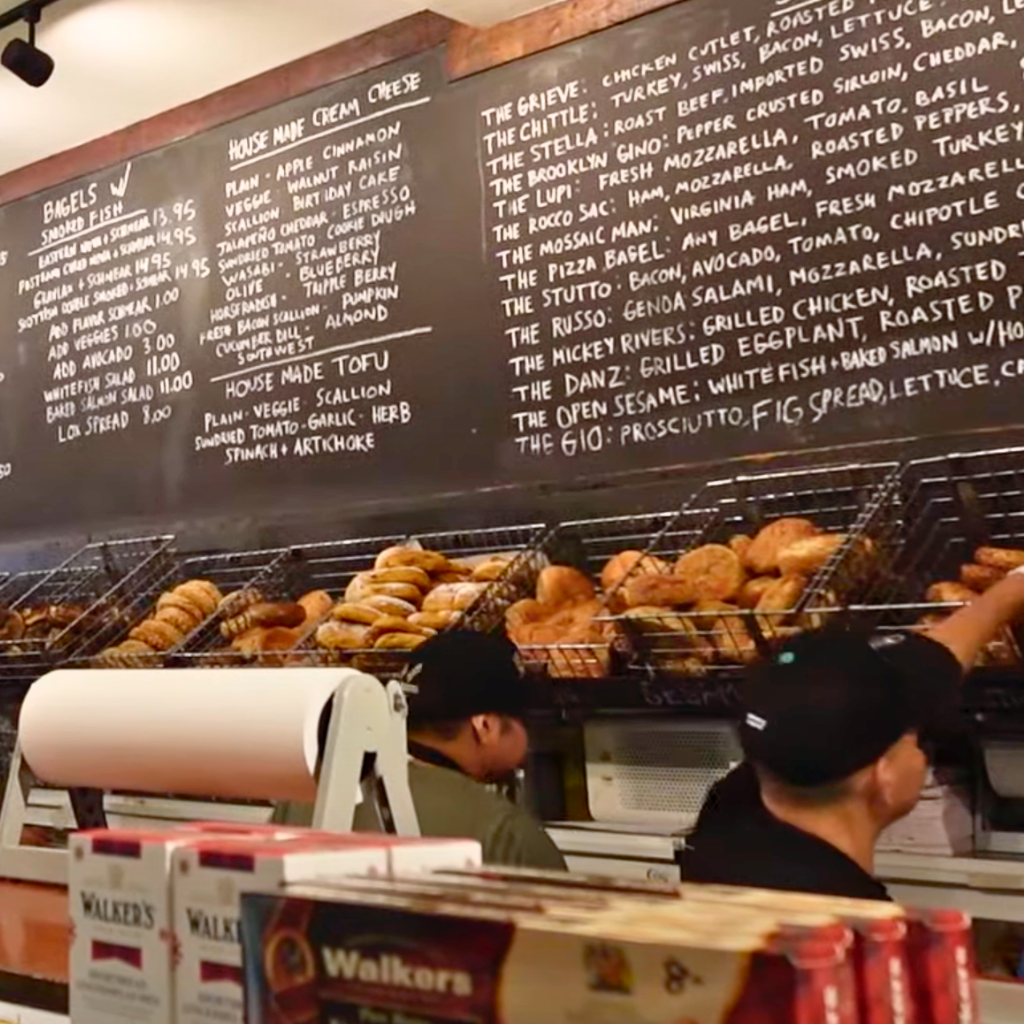 Interior of Tompkins Square Bagels showing a chalkboard menu and fresh bagels stacked behind the counter.