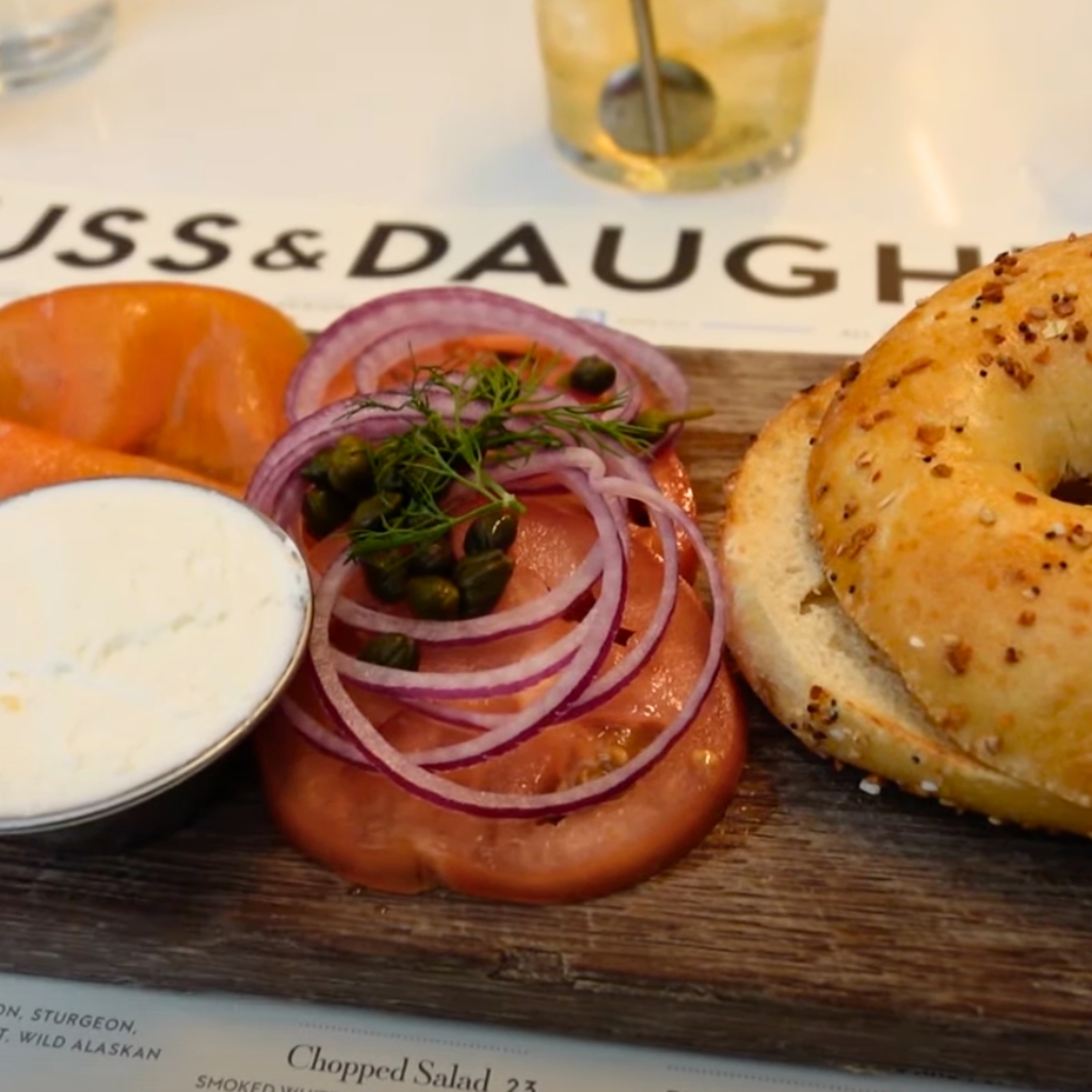 Bagel with lox, cream cheese, tomato, and onion served on a wooden board at Russ & Daughters in New York City.