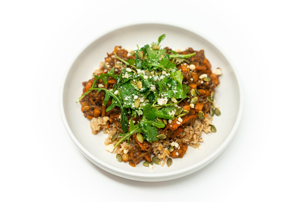 Ground lamb mole bowl served over brown rice, topped with lime-dressed arugula and cilantro, cotija cheese, and toasted pepitas.