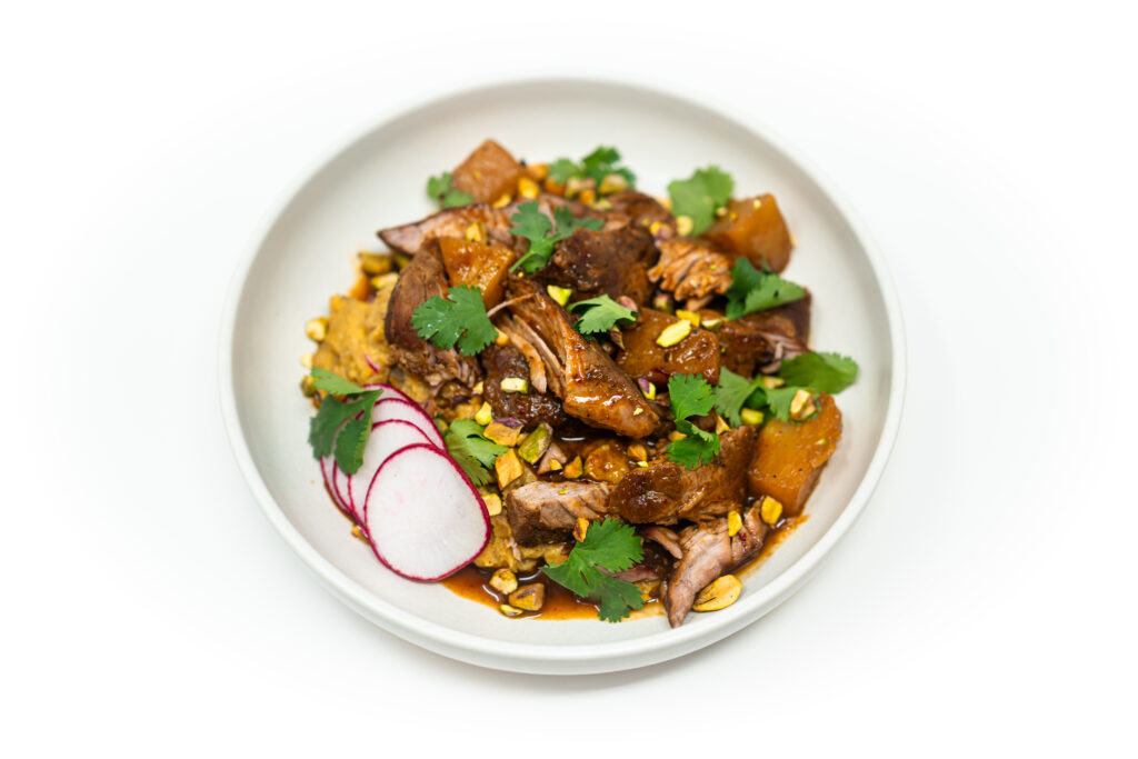 Pineapple-braised pork sirloin served over creamy mashed plantains, garnished with tender pineapple chunks and rich, reduced braising sauce in a rustic bowl.