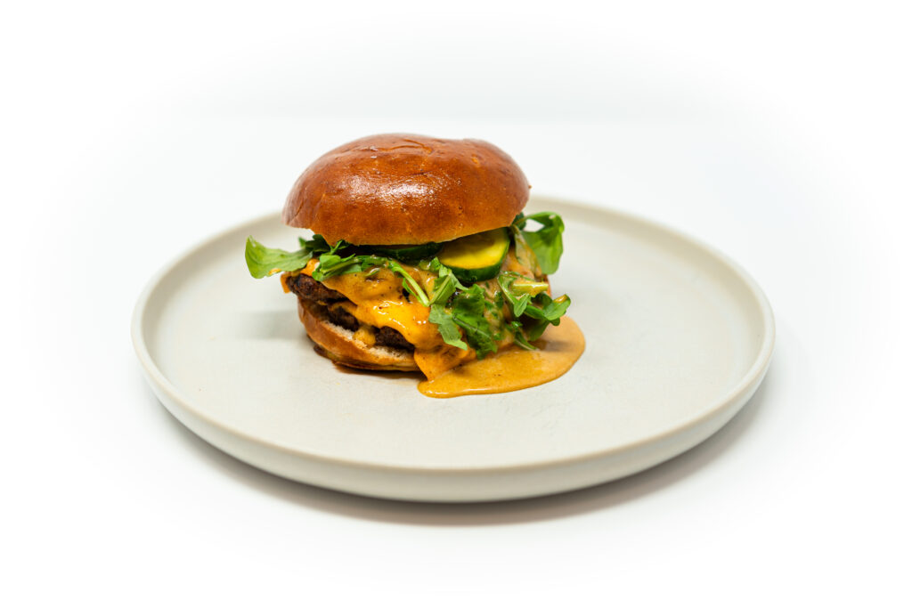 Short rib smash burger stacked with cheese, arugula, and bread and butter pickles.