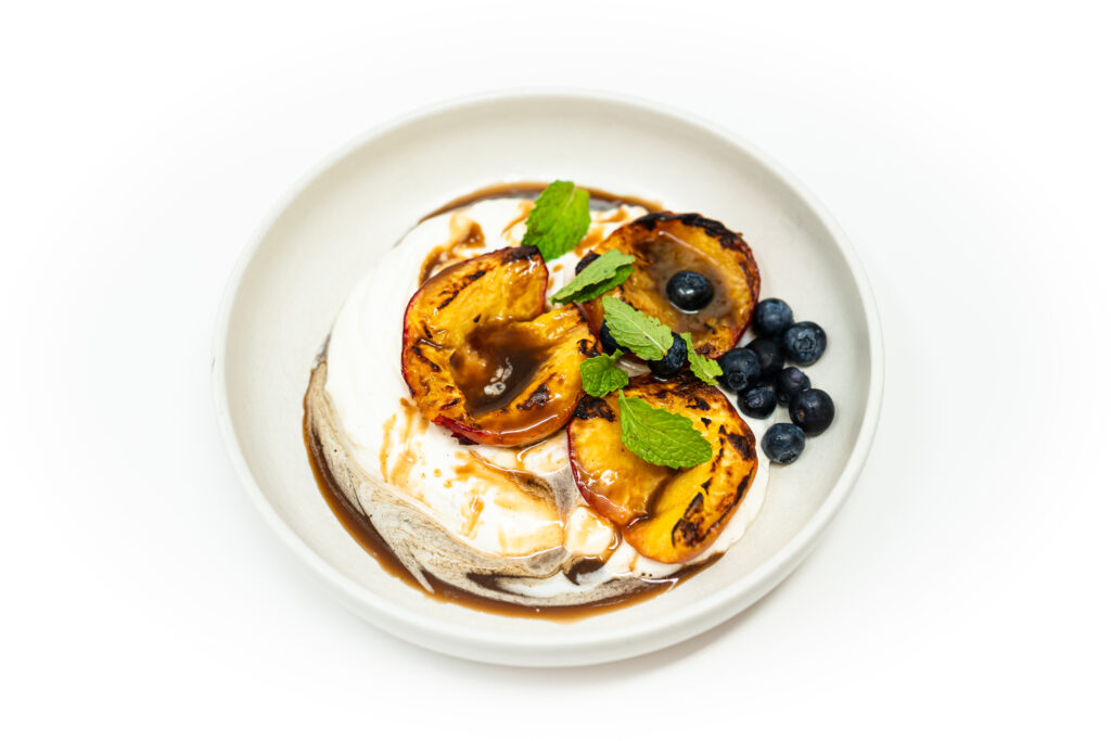 Grilled peach halves topped with bourbon caramel and a dollop of whipped vanilla bean mascarpone cream, garnished with blueberries and mint.