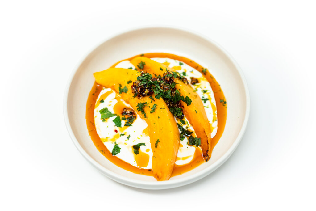 Roasted cantaloupe wedges served over whipped honey cottage cheese, topped with chili crisp and fresh basil on a white plate.