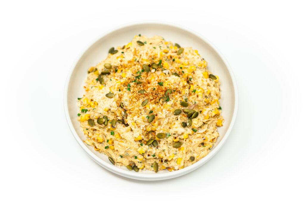 Bright plate of spaghetti squash esquites topped with cotija cheese, toasted pepitas, and lime, served in a white bowl on a clean background.