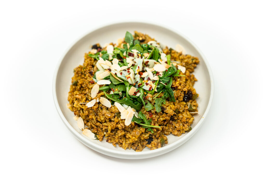 A vibrant Mediterranean rice bowl featuring golden saffron jasmine rice, spiced ground chicken with raisins and lemon zest, fresh arugula, toasted almonds, and mint, all drizzled with saffron oil.