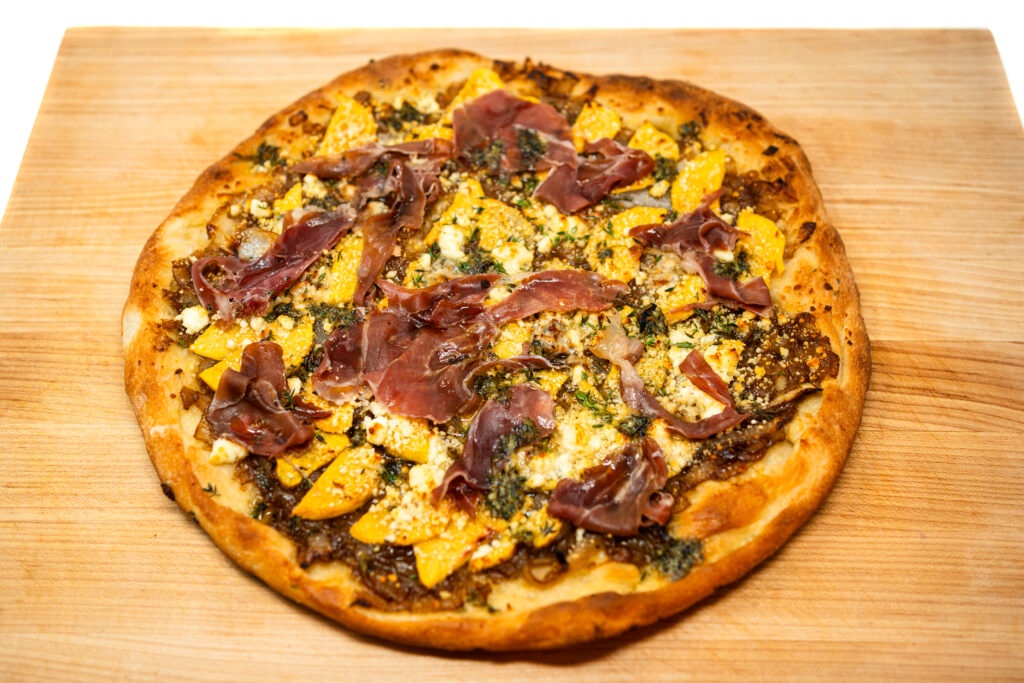 Close-up of peach, gorgonzola, and goat cheese pizza topped with caramelized onions, fresh prosciutto, thyme, and a drizzle of honey.