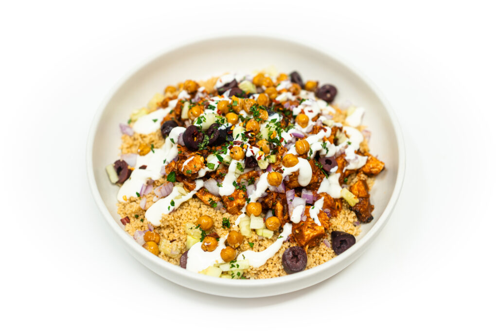Harissa-glazed diced chicken over couscous with toasted chickpeas, cucumber, red onion, olives, parsley, and a lemon tahini aioli drizzle.