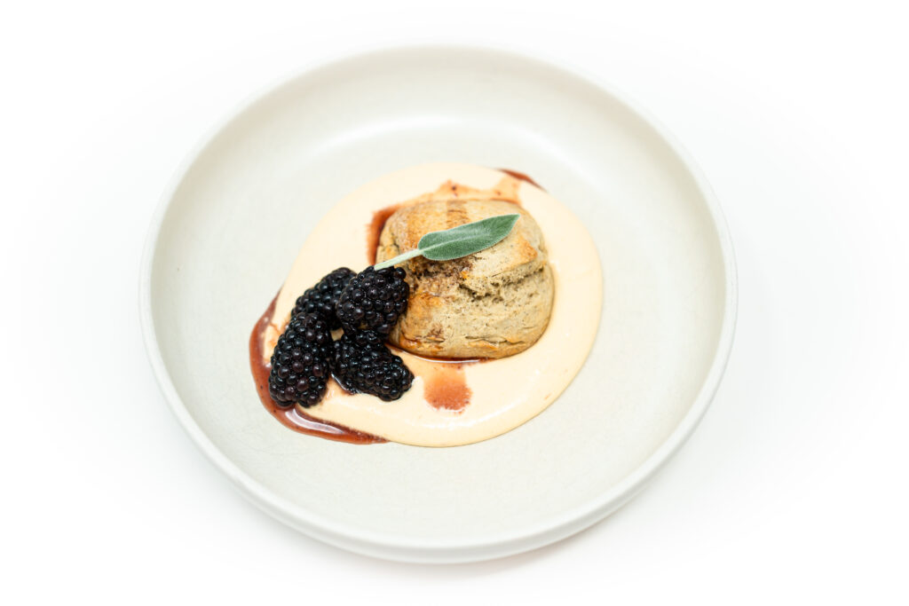 Golden vanilla bean shortcakes stacked with blackberry–sage syrup and topped with orange–vanilla whipped cream, garnished with fresh sage.