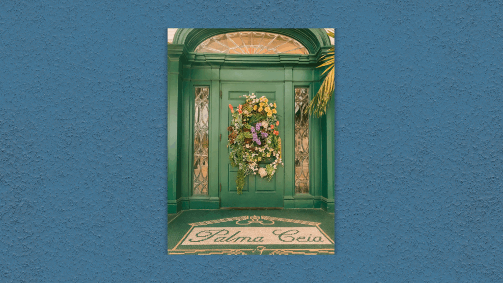 Green arched double doors at Palma Ceia Golf and Country Club, decorated with a large floral wreath of colorful flowers and greenery, with a mosaic tile entryway reading "Palma Ceia."