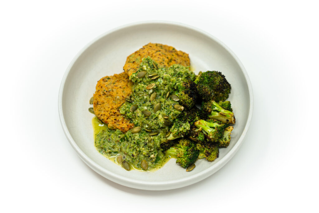 Crispy golden hake fish cakes served on a plate with smoky green pepper herb salsa and fresh lemon wedges.
