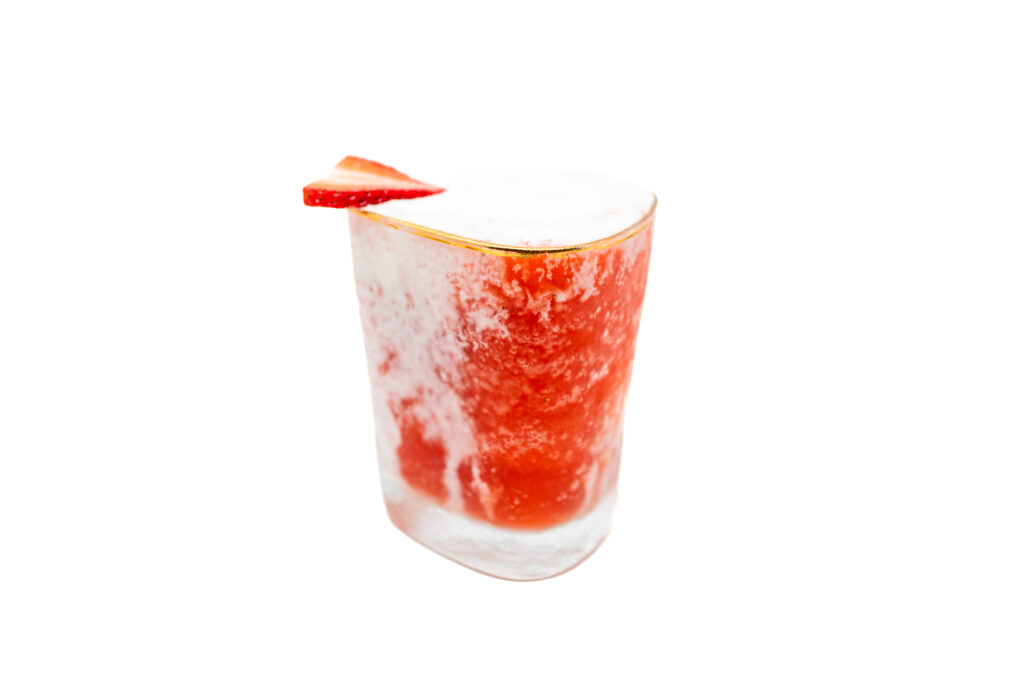 A vibrant strawberry and cream margarita in a clear glass with a fresh strawberry garnish, featuring a layered red and white swirl.