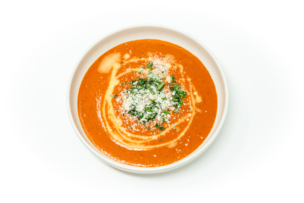 Bowl of roasted Roma tomato and garlic gazpacho topped with parsley and Parmesan, drizzled with olive oil, served chilled.