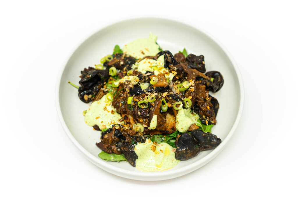 Crispy fried masa polenta cakes topped with wild mushrooms, avocado cilantro cream, and fresh arugula on a white plate.