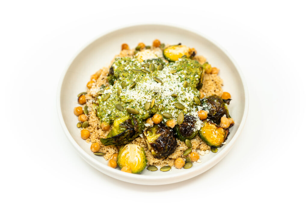 Cumin couscous bowl topped with roasted Brussels sprouts, crispy chickpeas, and drizzled with a vibrant charred poblano herb sauce.