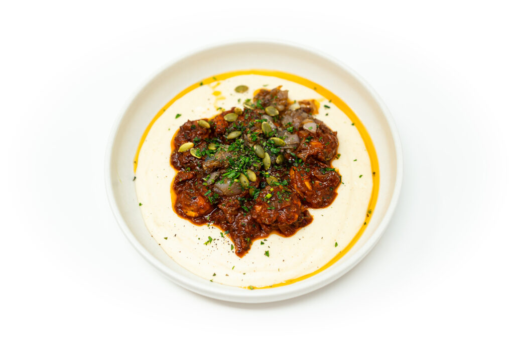 Bowl of chipotle shrimp in smoky tomato sauce served over creamy masa polenta, topped with toasted pepitas and fresh herbs.