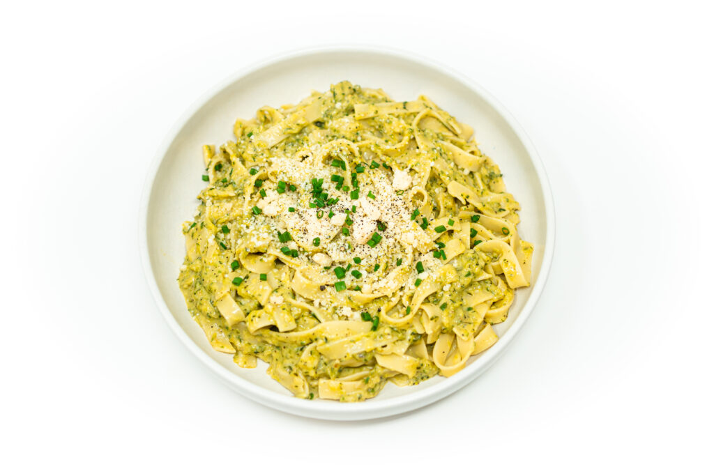 Creamy zucchini Alfredo pasta topped with Parmesan cheese and chopped chives, served in a white bowl.