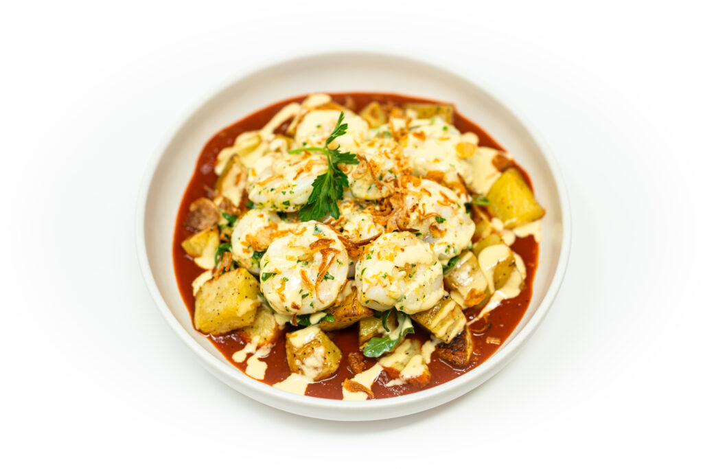 A plate of patatas bravas with shrimp topped with spicy tomato sauce, garlic aioli, fried onions, and fresh parsley.