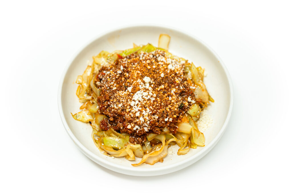 A bowl of deconstructed cabbage rolls with charred cabbage ribbons, rich tomato-braised beef and pork sauce, and Pecorino Romano cheese.