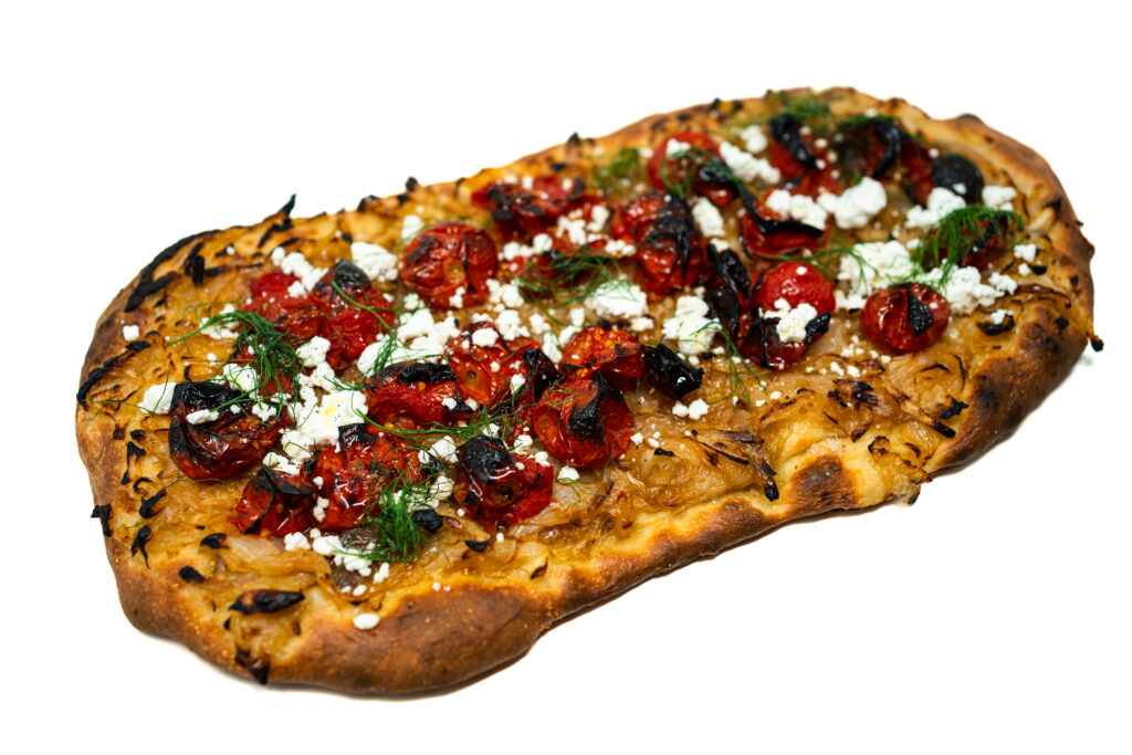 Flatbread topped with caramelized onion, roasted cherry tomatoes, goat cheese crumbles, and fennel fronds on a golden, crisp crust