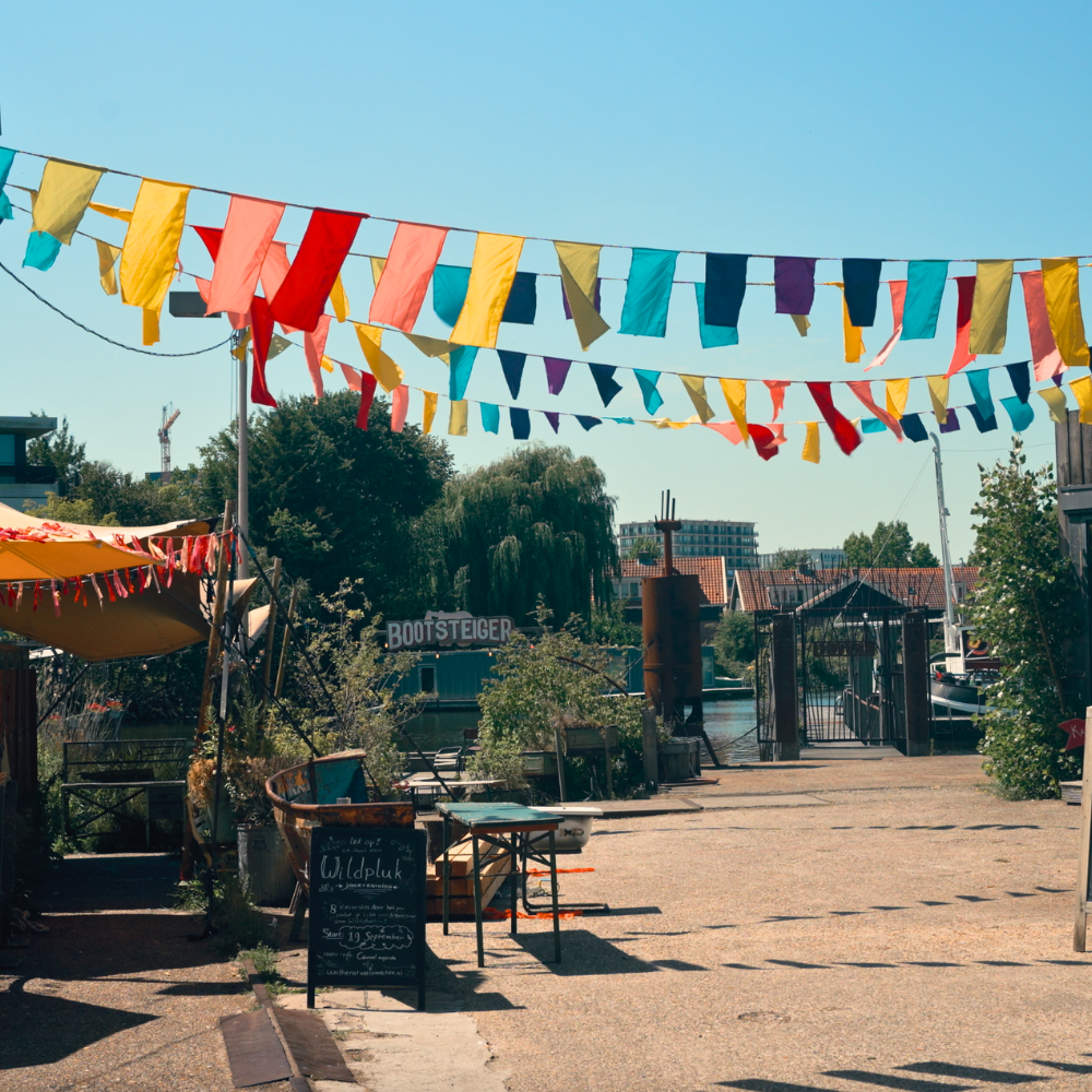 Cafe de Ceuvel in Amsterdam, a creative waterfront café built on houseboats with colorful flags and sustainable design.