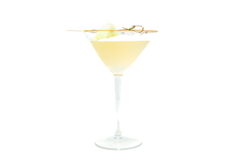 A chilled honeydew tequila martini in a stemmed glass with a honeydew garnish on a skewer, showing its pale green hue.