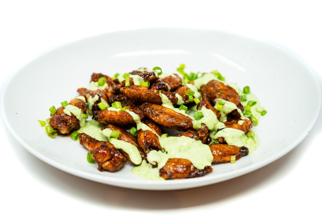 A platter of crispy honey chipotle buffalo wings drizzled with green onion crema and topped with chopped scallions.