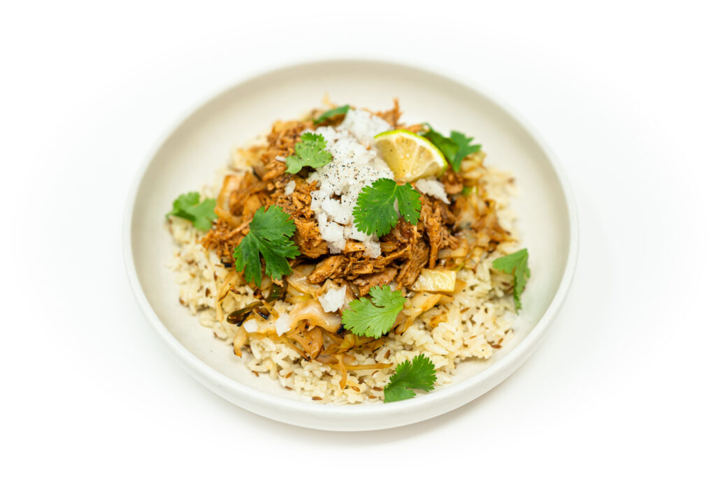 Bowl of honey chipotle chicken served with toasted cumin rice and charred cabbage, garnished with cilantro, diced onion, and lime wedges.