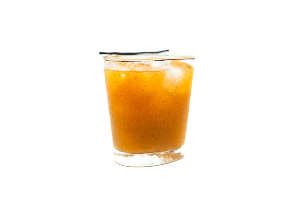 A glass of vanilla bean margarita with ice cubes and a vanilla bean garnish