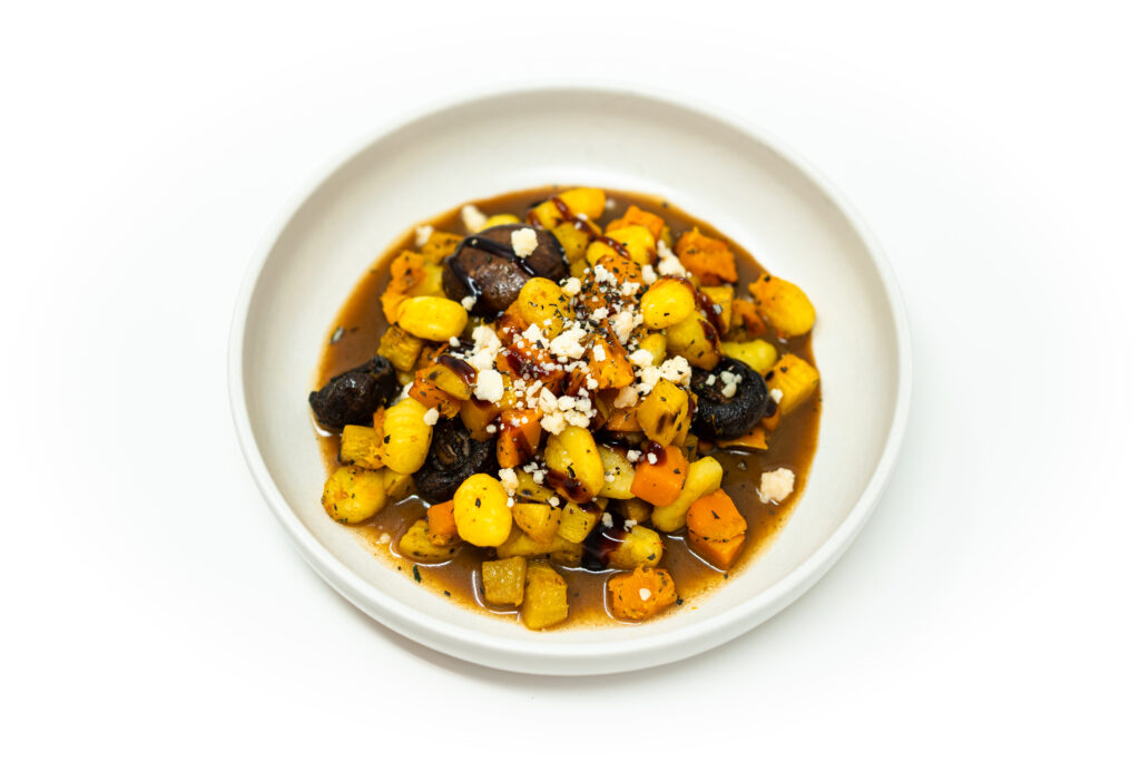 Sheet pan gnocchi with roasted butternut squash and golden beets on a white plate, finished with brown butter muscovado sauce, balsamic glaze, goat cheese, and thyme.