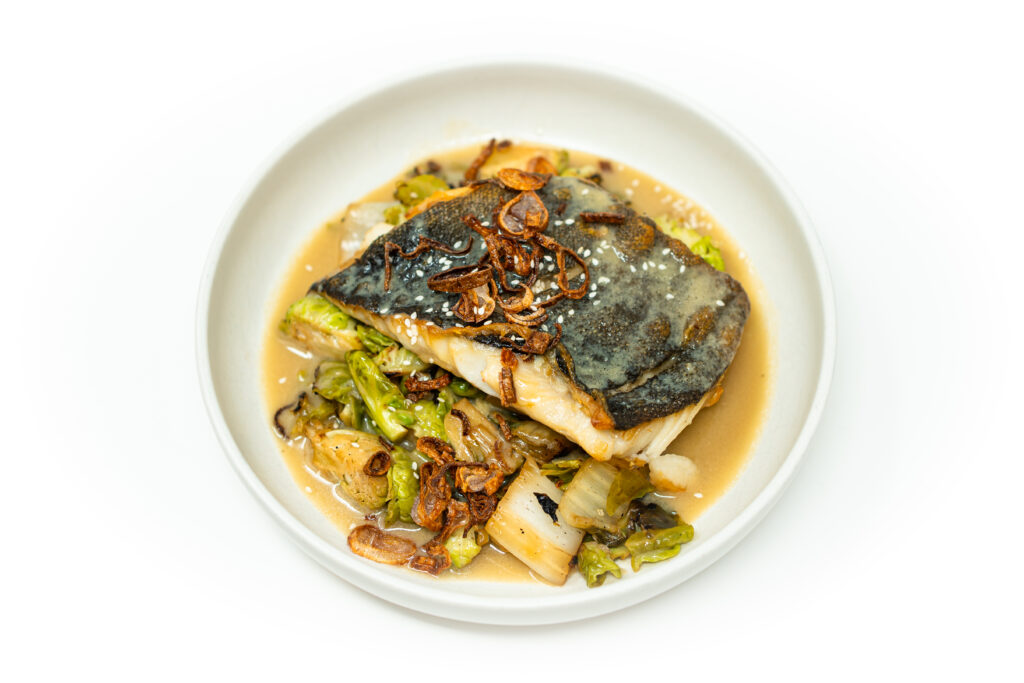 Pan-seared black cod with white wine miso sauce, charred Brussels sprouts and bok choy, topped with crispy fried shallots