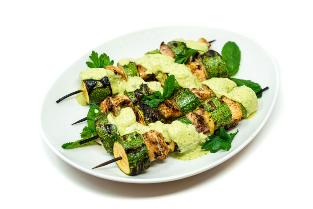 Herb-marinated shark and zucchini skewers on a plate, topped with herbed butter and served with a creamy herb yogurt sauce.