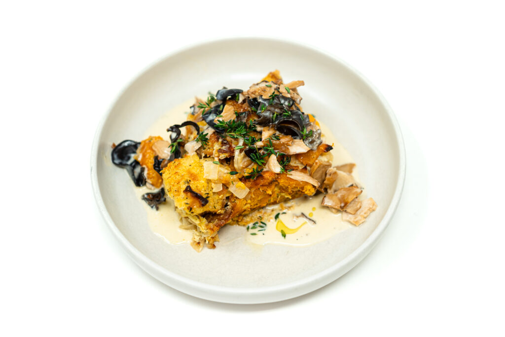 Close up plate of savory butternut squash and ciabatta bread pudding topped with creamy wild mushrooms and fresh thyme on a white dish.