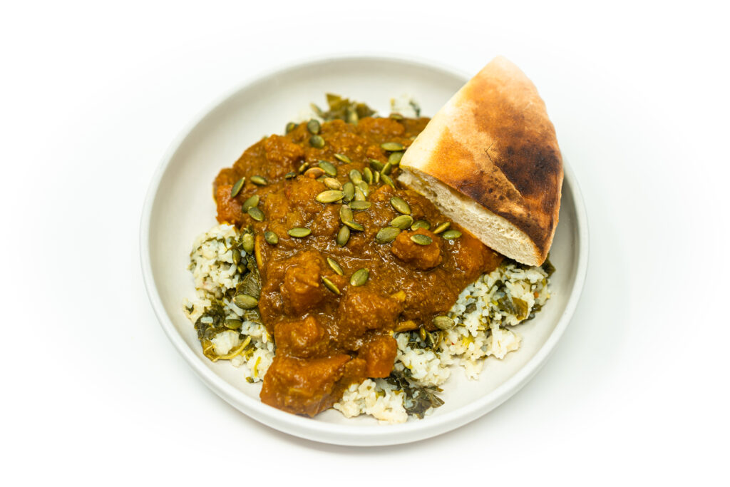 A bowl of calabaza curry with lemongrass and coconut milk served over callaloo rice, garnished with herbs and pepitas.