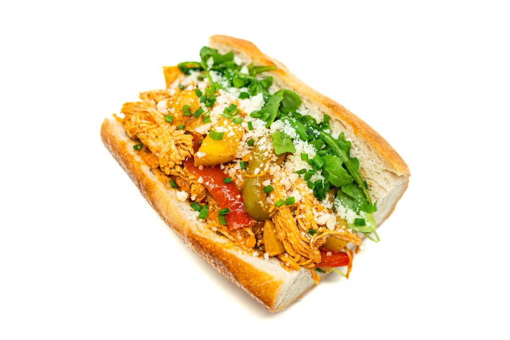 Close-up of a shredded buffalo chicken and potato hoagie with golden potatoes, caramelized peppers, and melted cheese on a toasted roll.