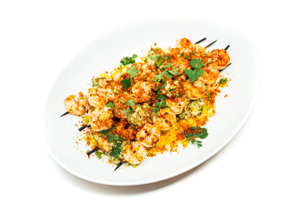 Grilled shrimp topped with melting herbed butter and a paprika breadcrumb crumble, garnished with cilantro and lime wedges on a rustic plate.