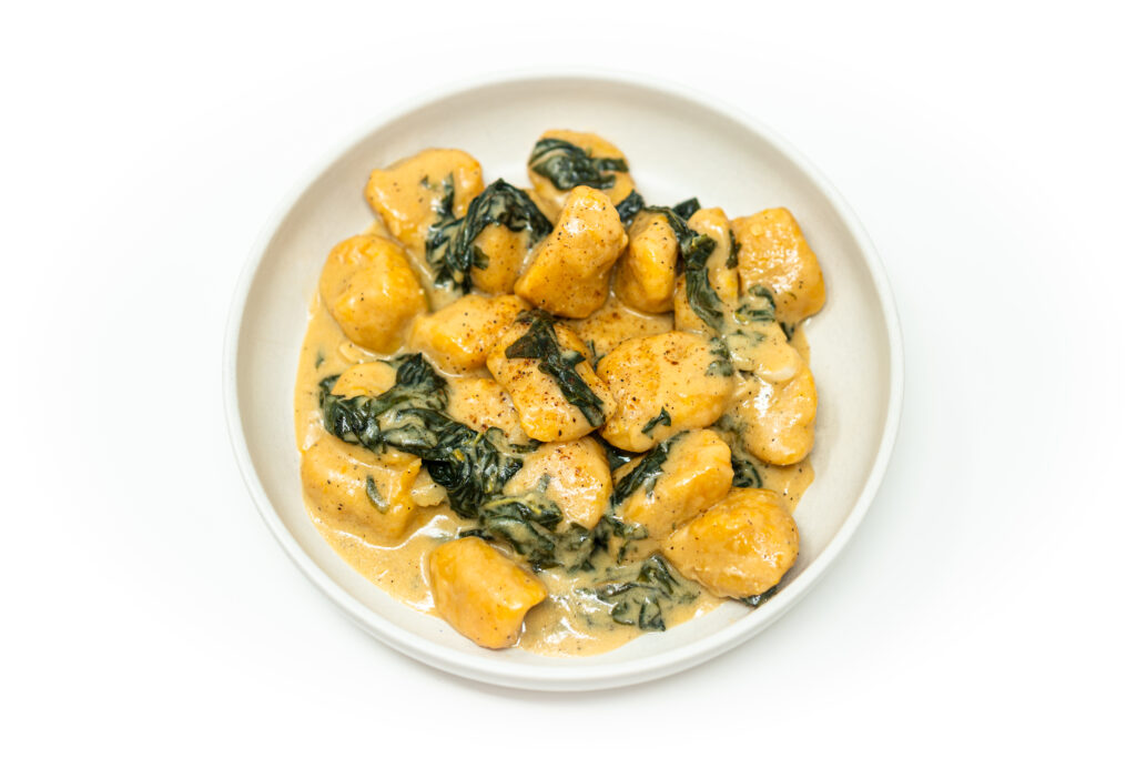 A plate of golden calabaza gnocchi tossed in a miso brown butter sauce with sautéed callaloo and garlic, topped with nutmeg and Parmesan.