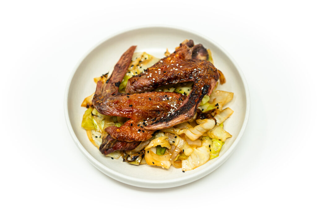 Sambal oelek honey duck wings glazed with spicy honey sauce, topped with sesame seeds and sesame oil drizzle