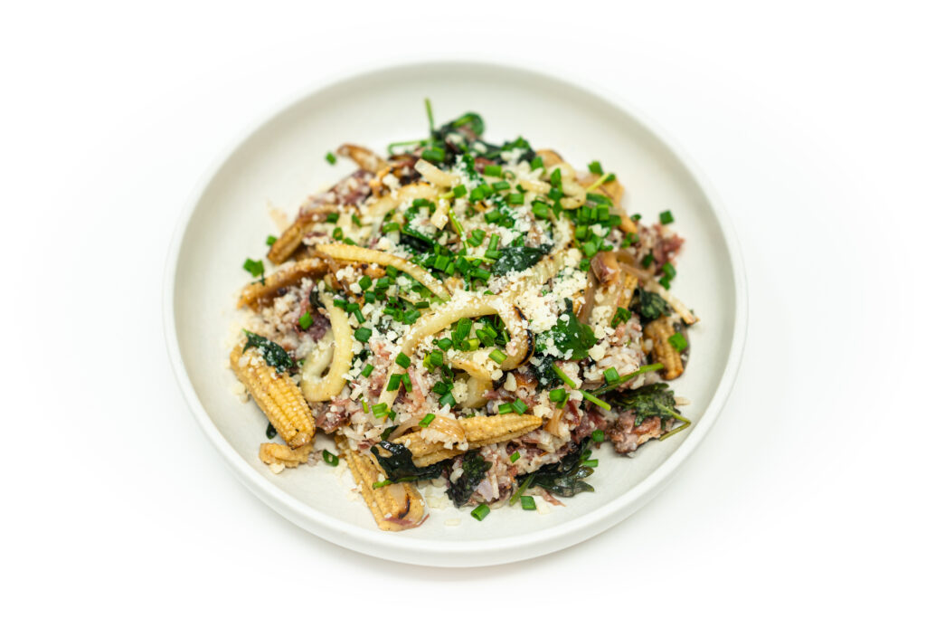 A warm plate of braised ham with caramelized fennel, baby corn, and greens, drizzled with citrus shallot vinaigrette and topped with shaved Parmesan.