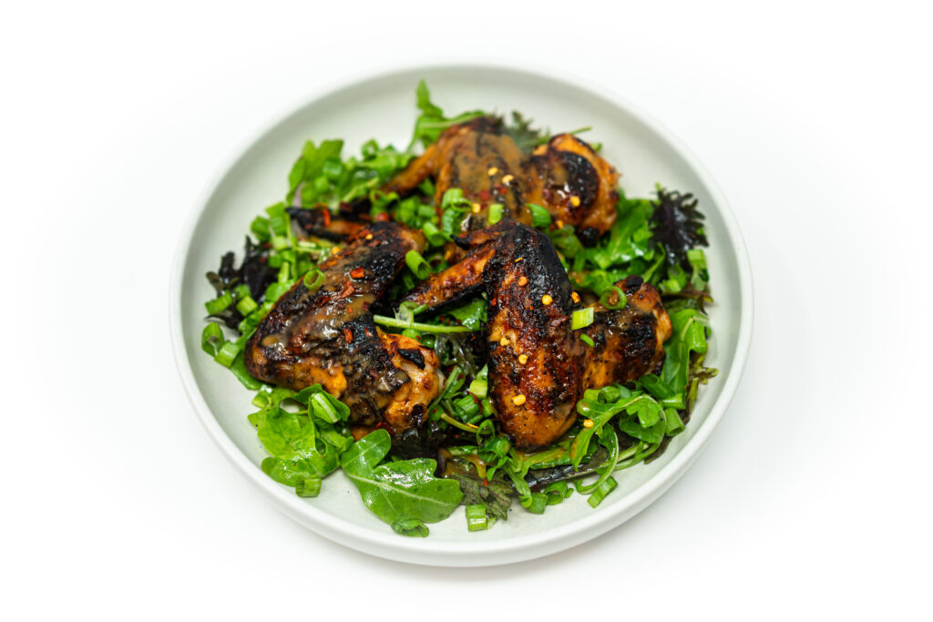 Whole grilled chicken wings glazed with citrus brown sugar mojo sauce, garnished with herbs and green onions on a dark plate